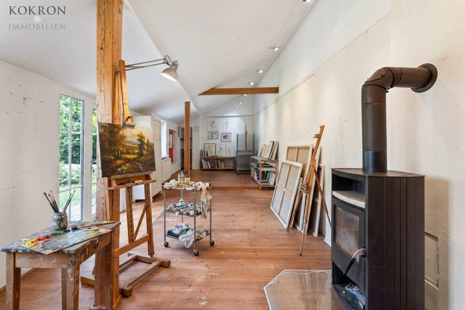 Helles Atelier mit Holzboden, einem gemütlichen Holzofen und großen Fenstern mit Blick ins Grüne.