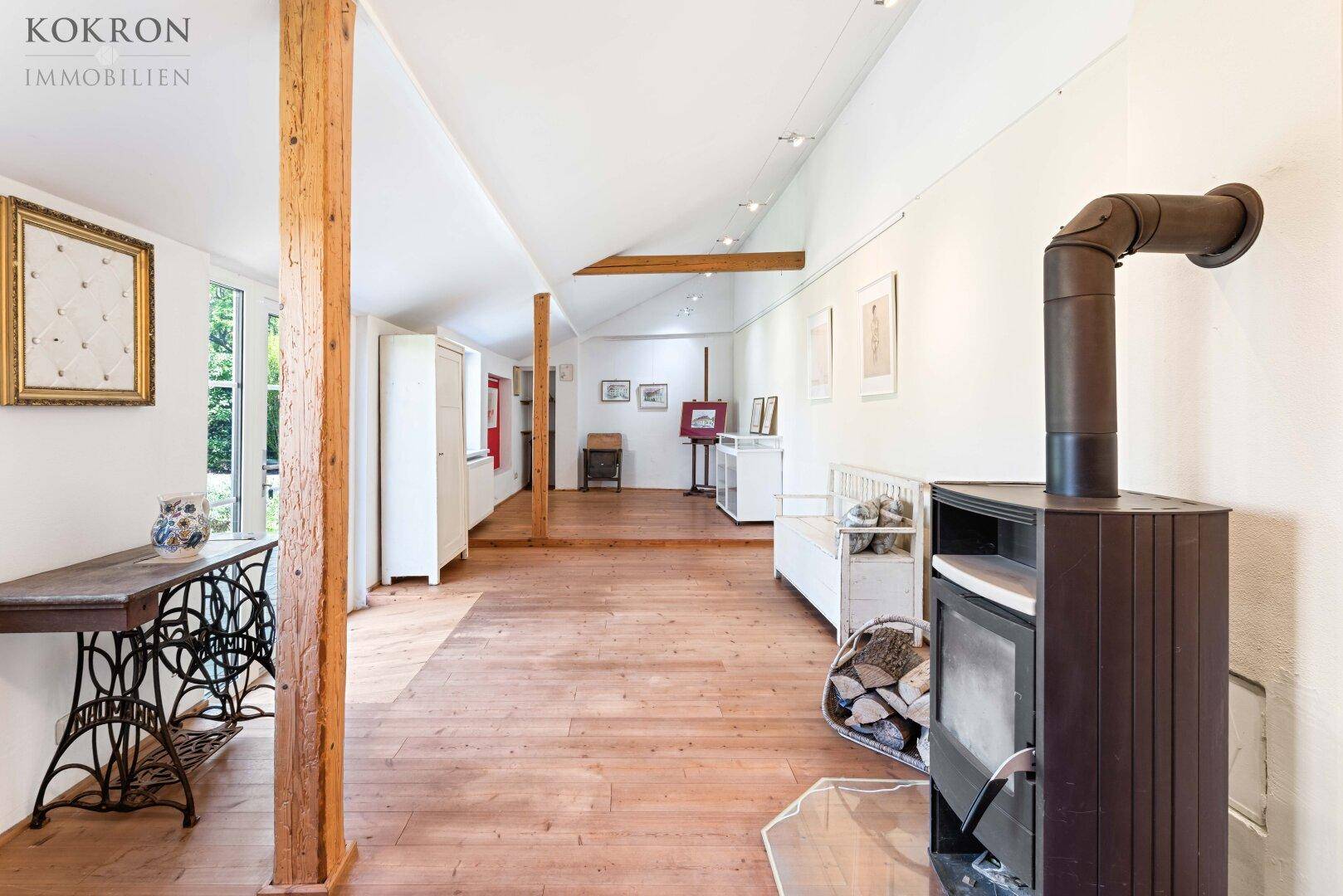 Geräumiges Atelier mit rustikalem Holzboden, einem Holzofen und sichtbaren Deckenbalken für kreative Arbeit.
