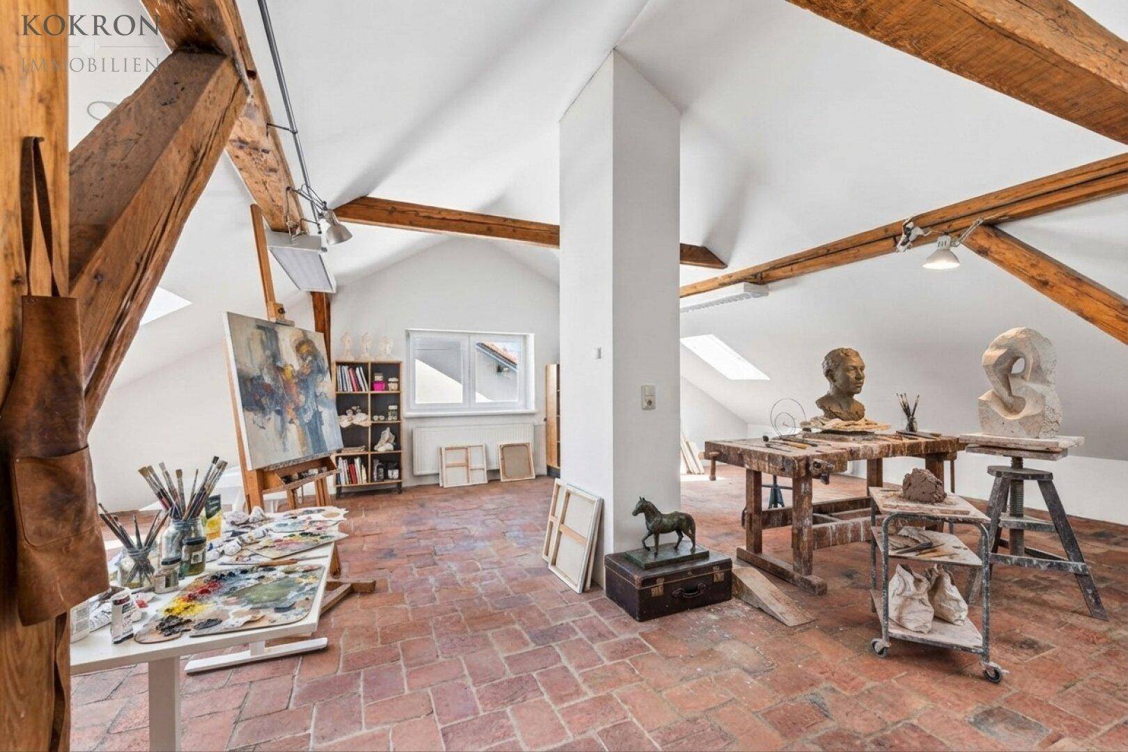 Kreativer Arbeitsbereich im Dachgeschoss mit Terrakottafliesen, sichtbaren Holzbalken und viel Tageslicht.