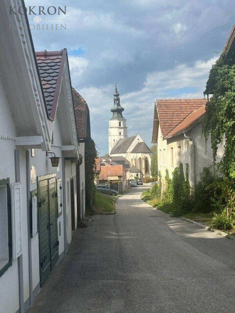 Historische Dorfstraße mit traditionellen Häusern und Blick auf eine markante Kirche unter bewölktem Himmel.