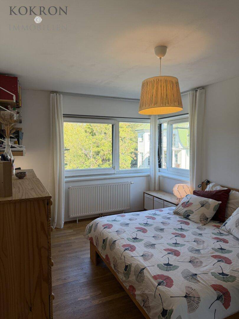 Helles Schlafzimmer mit Holzboden und großen Fenstern, bietet einen ruhigen Blick ins Grüne.