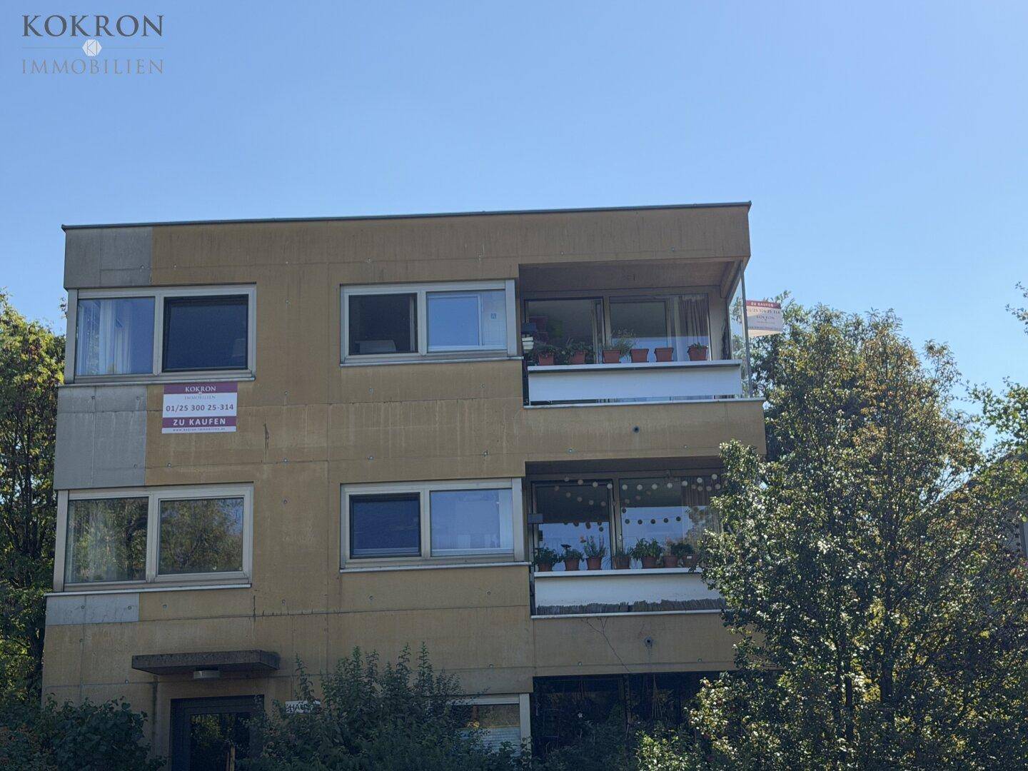 Mehrfamilienhaus mit moderner Architektur, großen Fenstern und Balkonen, umgeben von viel Grün.
