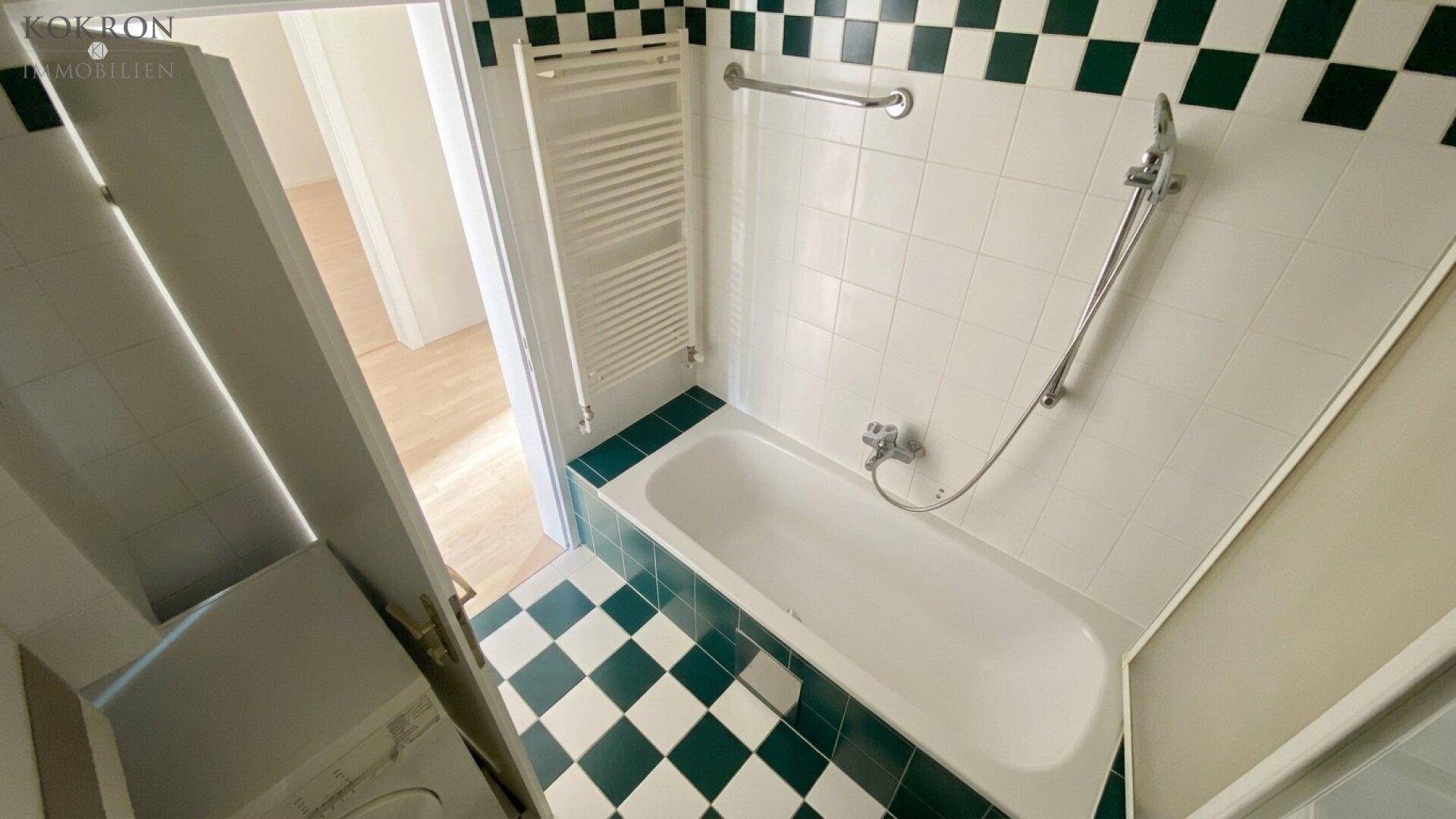 Badezimmer mit Badewanne, grün-weiß karierten Fliesen und einem beheizten Handtuchhalter.
