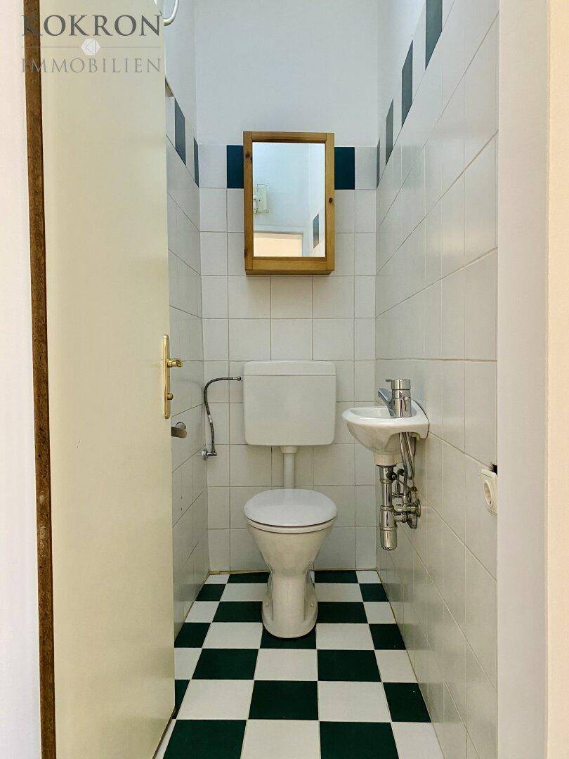 Kleines Gäste-WC mit Toilette, Waschbecken und einem Holzspiegel, ausgestattet mit karierten Fliesen.