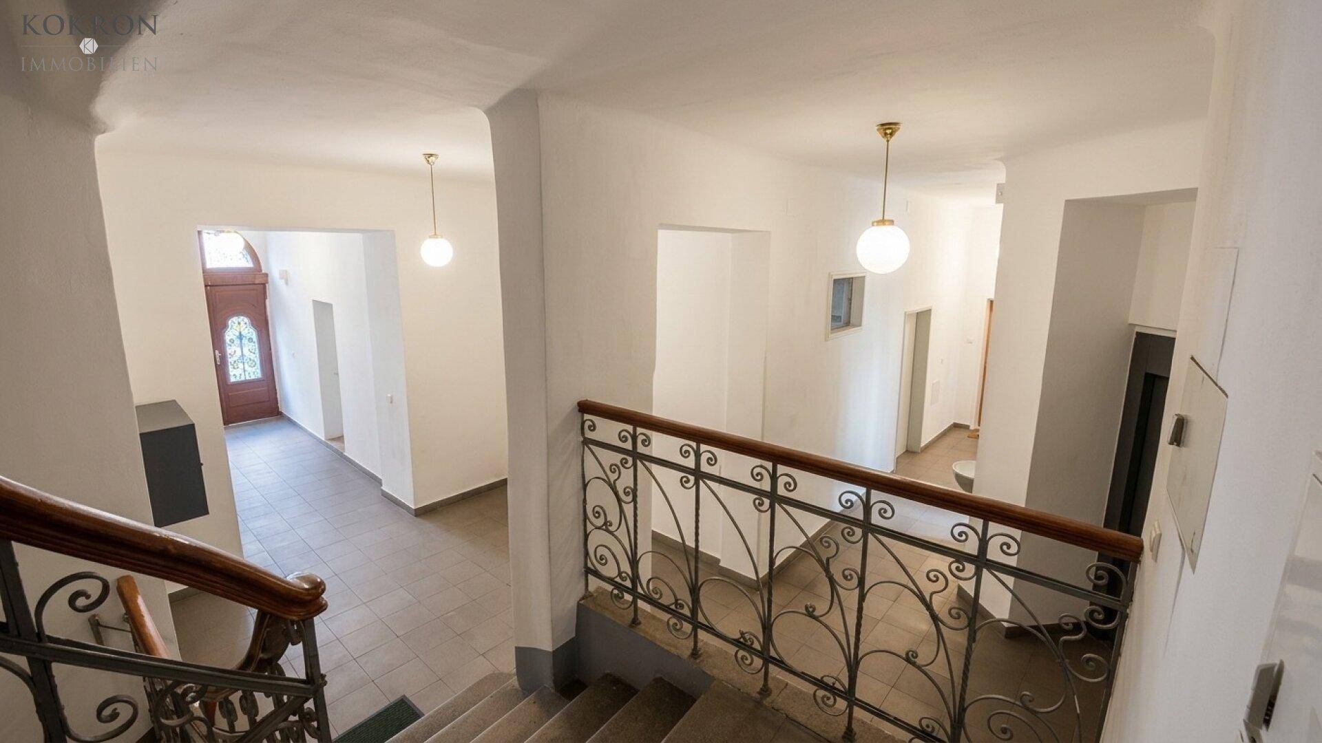 Historisches Treppenhaus mit schmiedeeisernem Geländer und hohen Decken in einem Altbau.