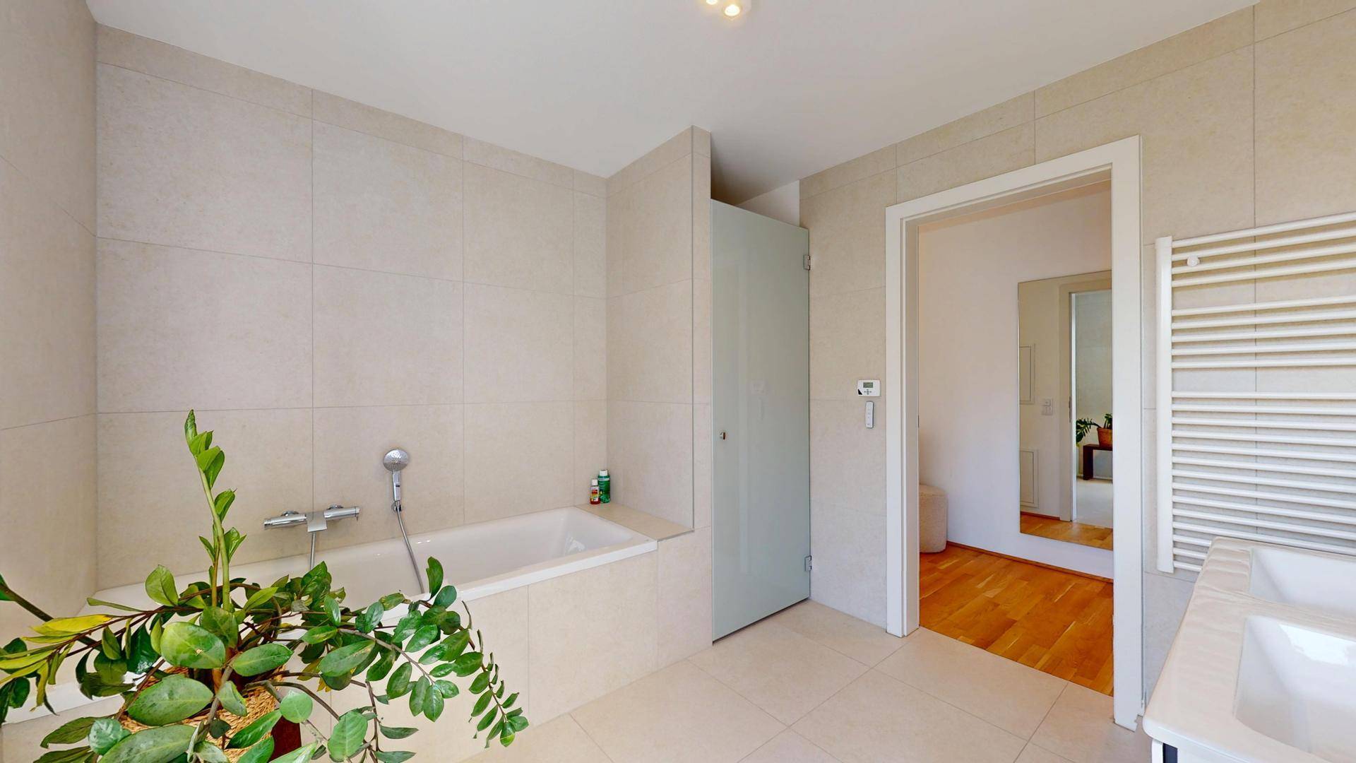 Helles Badezimmer mit Badewanne, Fliesenboden und beheiztem Handtuchhalter.