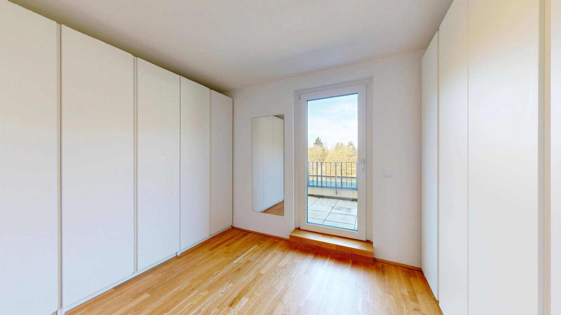 Schlafzimmer mit Einbauschränken, Holzboden und Zugang zu einem Außenbereich.