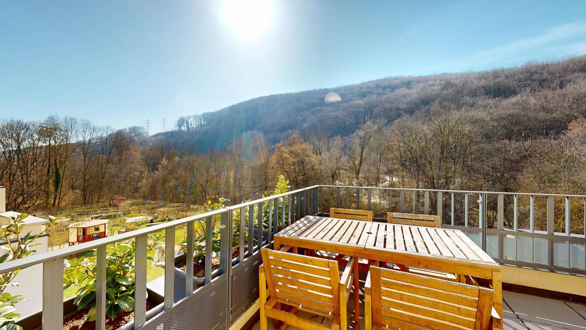 Sonniger Außenbereich mit Holztisch und Stühlen, umgeben von grünen Hügeln.