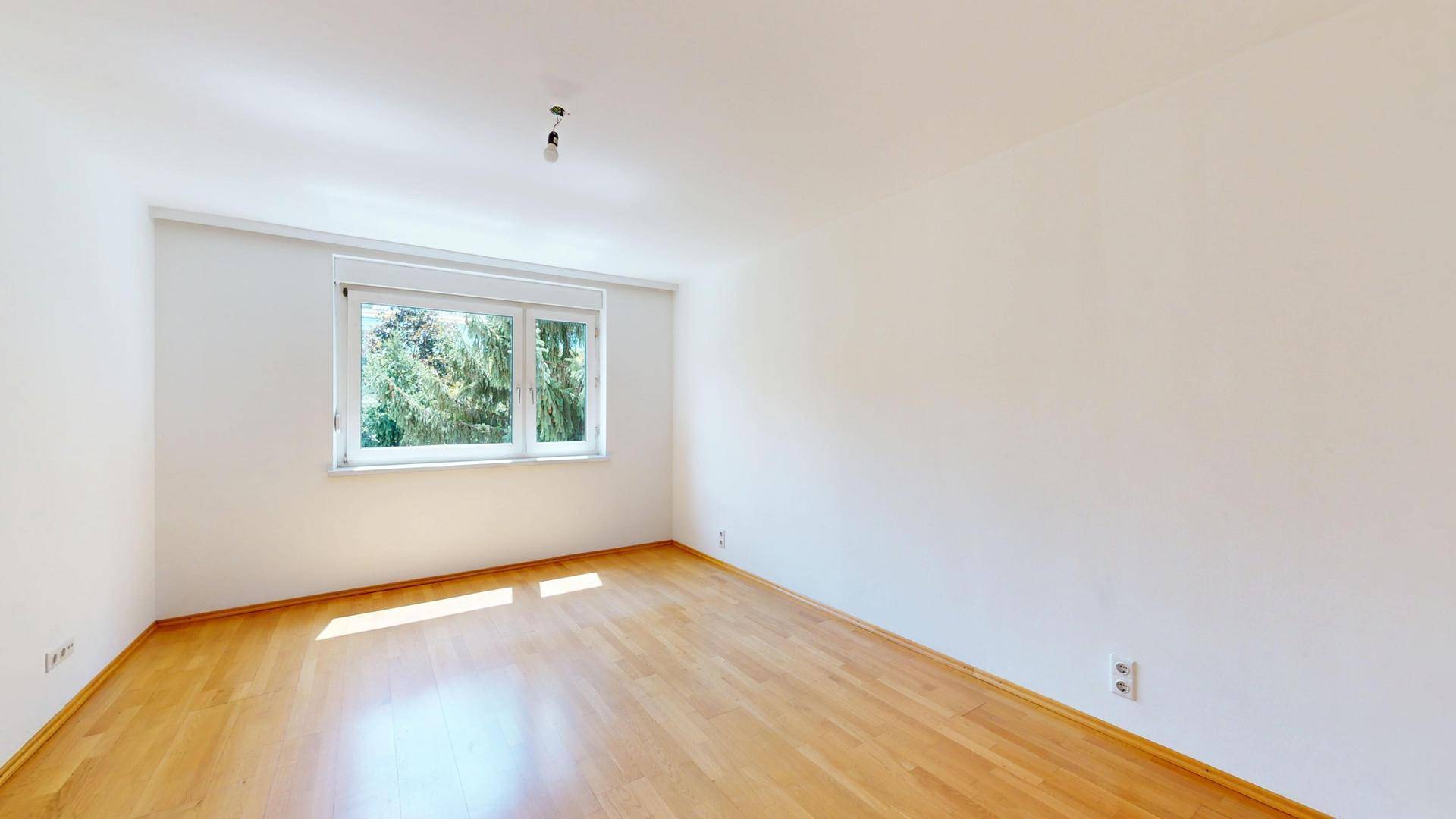 Sonniges Zimmer mit Parkettboden und weitem Blick durch das große Fenster.