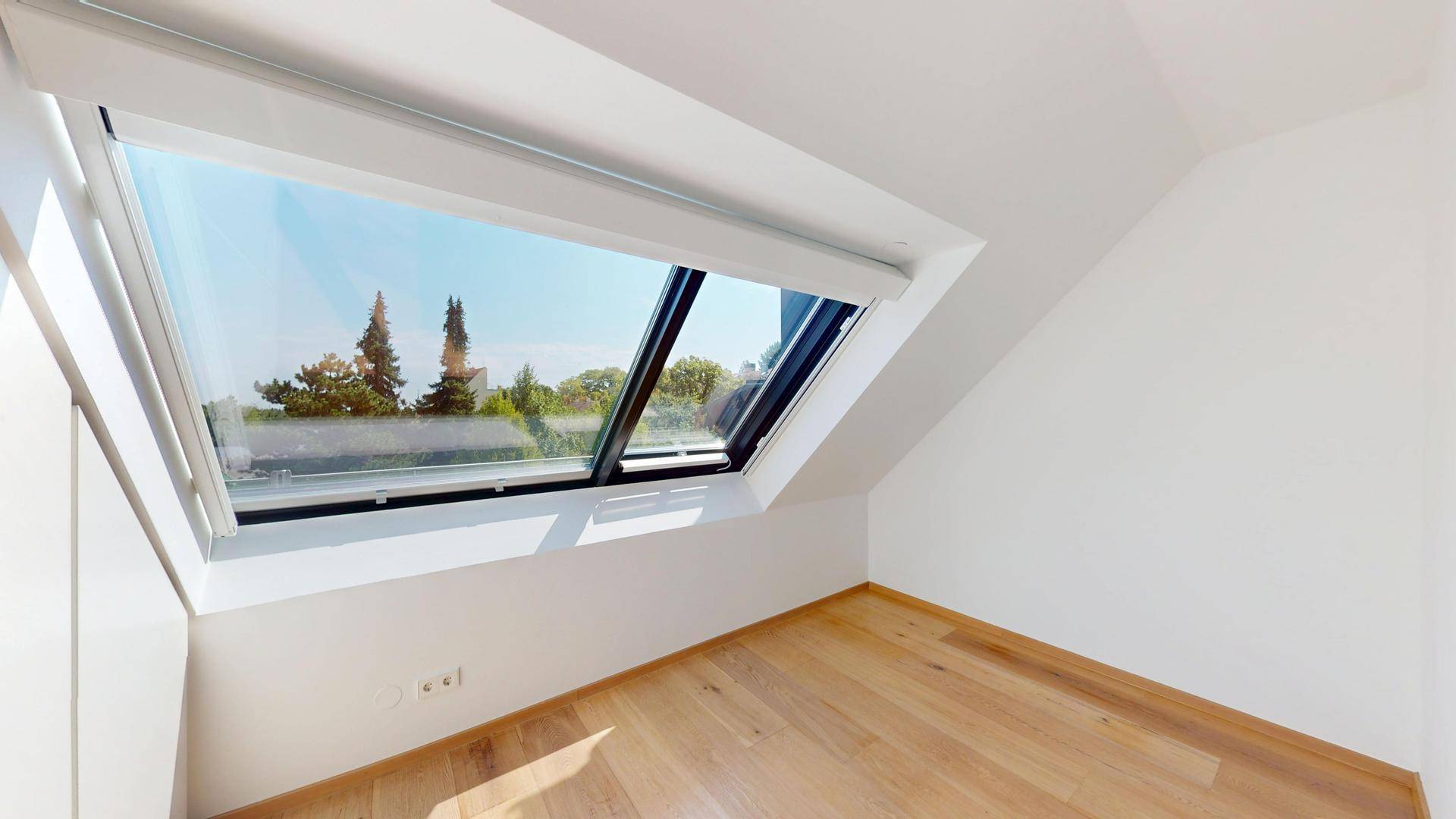 Geräumiges Schlafzimmer mit Holzboden, weißen Wänden und einem großen Dachfenster für viel Tageslicht.