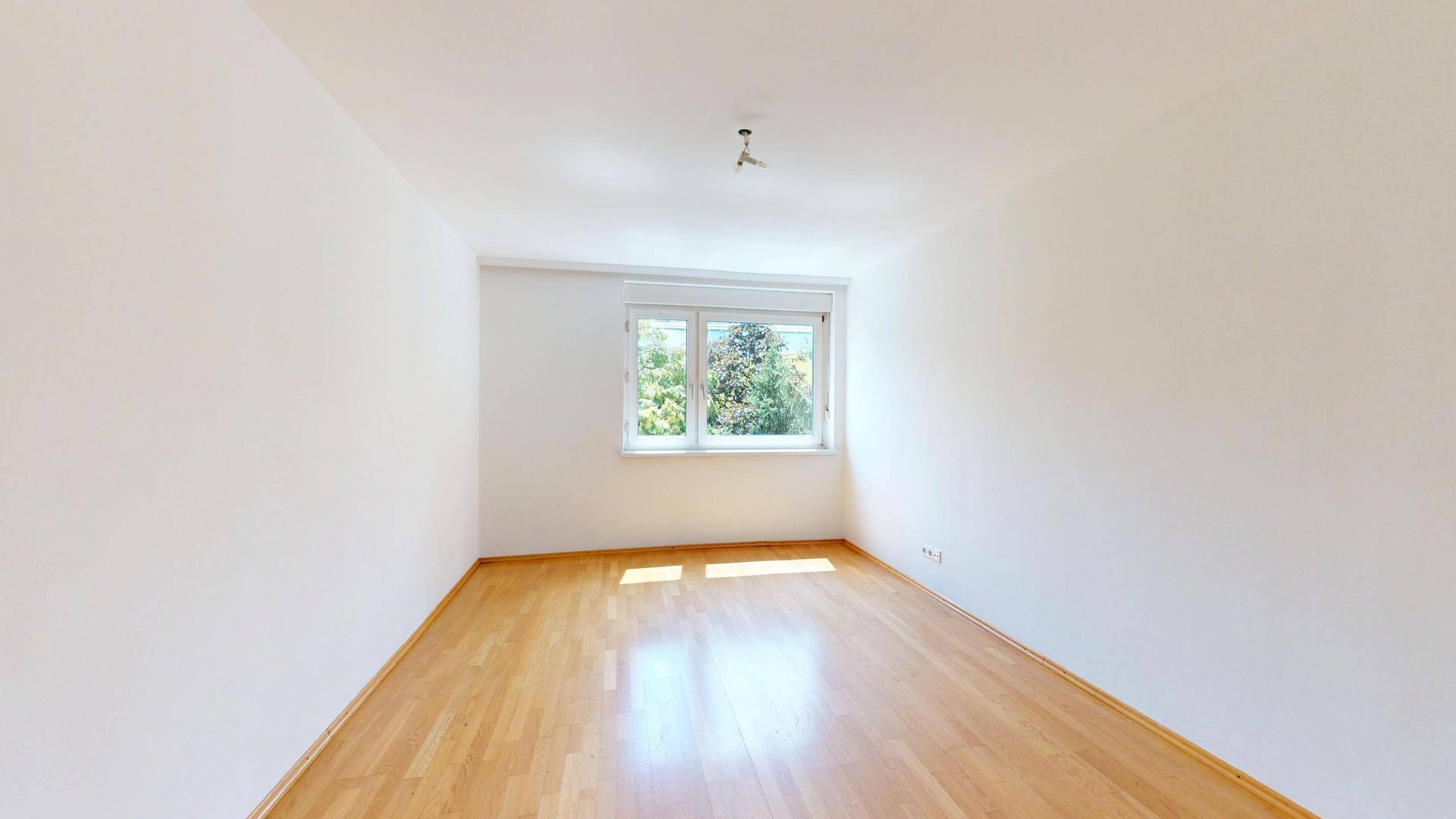 Helles Schlafzimmer mit Holzparkett und großem Fenster mit Blick ins Grüne.