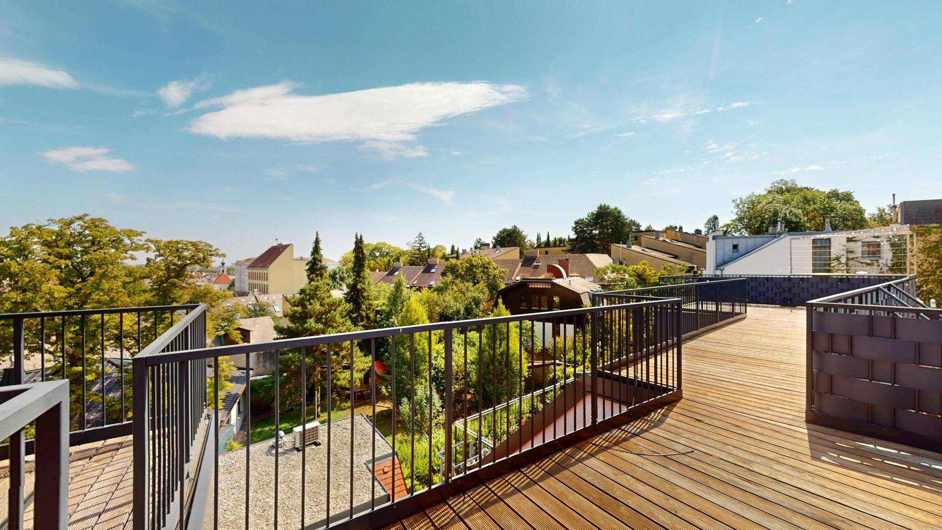 Geräumige Dachterrasse mit Holzboden und weitem Blick über die grüne Umgebung und Dächer.