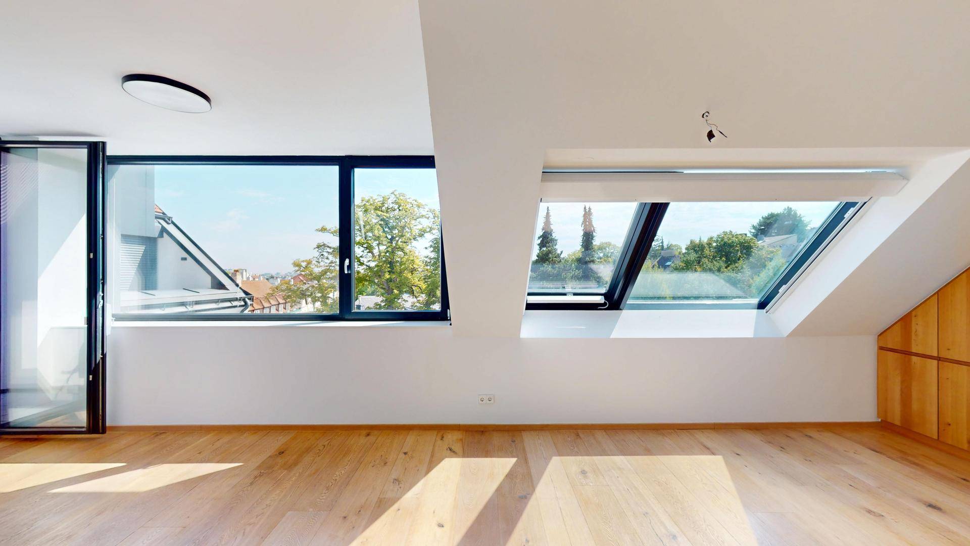 Lichtdurchfluteter Wohnbereich im Dachgeschoss mit Holzboden und weitem Ausblick durch große Fenster.