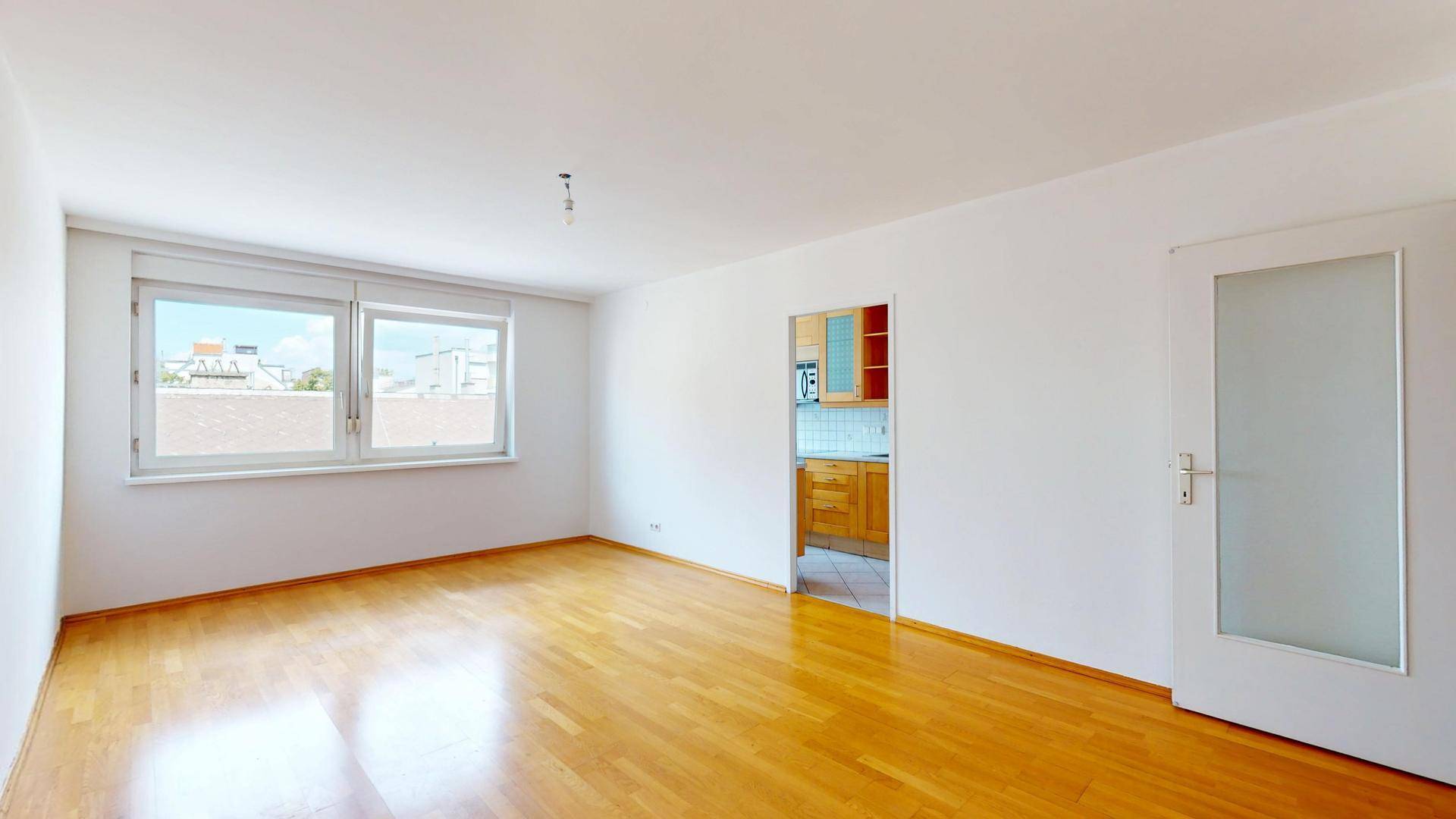 Wohnzimmer mit Parkettboden und offener Verbindung zu einer angrenzenden Küche.