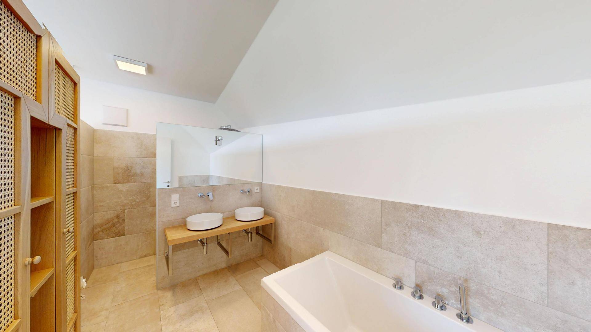Modernes Badezimmer mit Doppelwaschbecken, Badewanne und hellen Fliesen in Natursteinoptik.