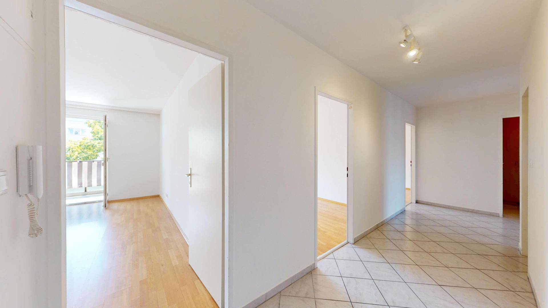 Heller Flur mit Fliesenboden und Zugang zu einem Zimmer mit Balkon.