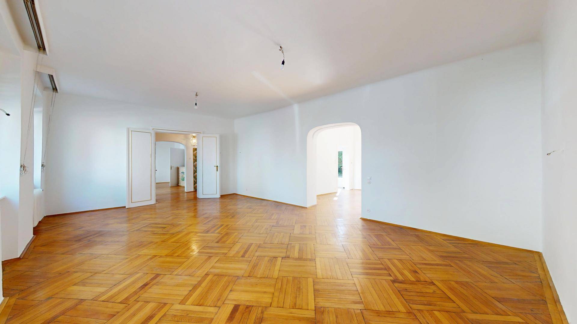 Helles Wohnzimmer mit klassischem Parkettboden und Zugang zu weiteren Räumen, ideal für offene Wohnkonzepte.