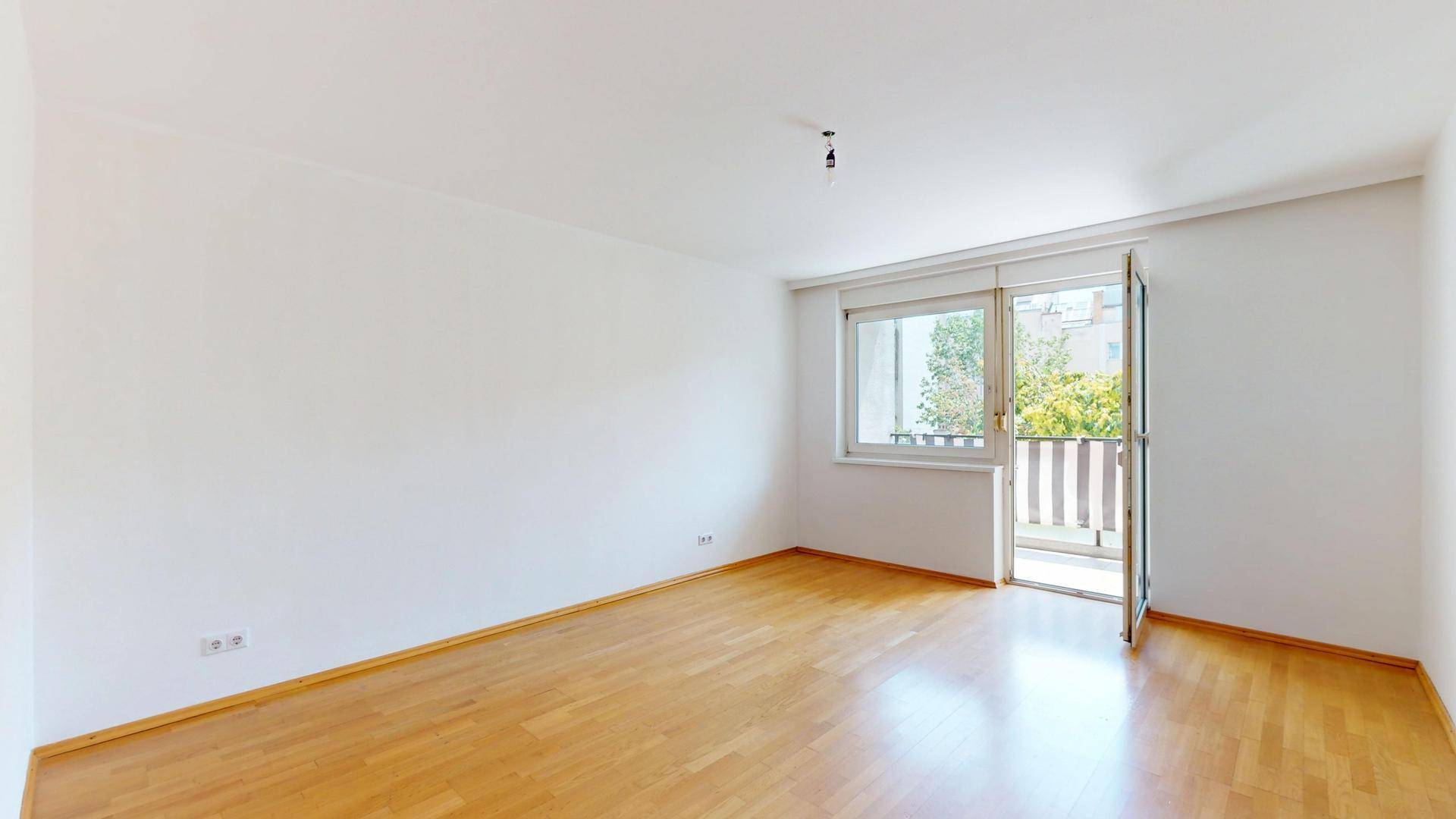 Geräumiges Zimmer mit Parkettboden und direktem Zugang zum sonnigen Balkon.