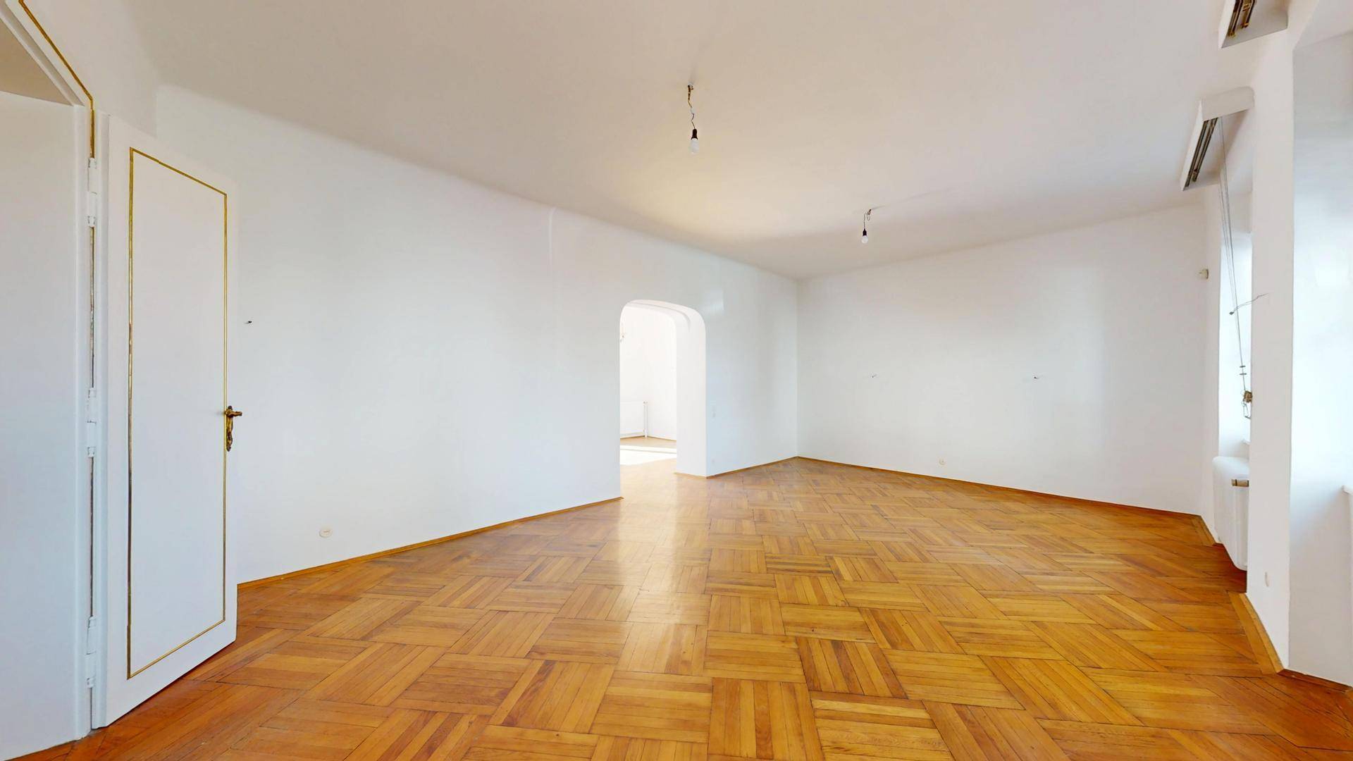 Geräumiges, leeres Wohnzimmer mit Fischgrätparkett und weiß gestrichenen Wänden, bereit zur individuellen Gestaltung.