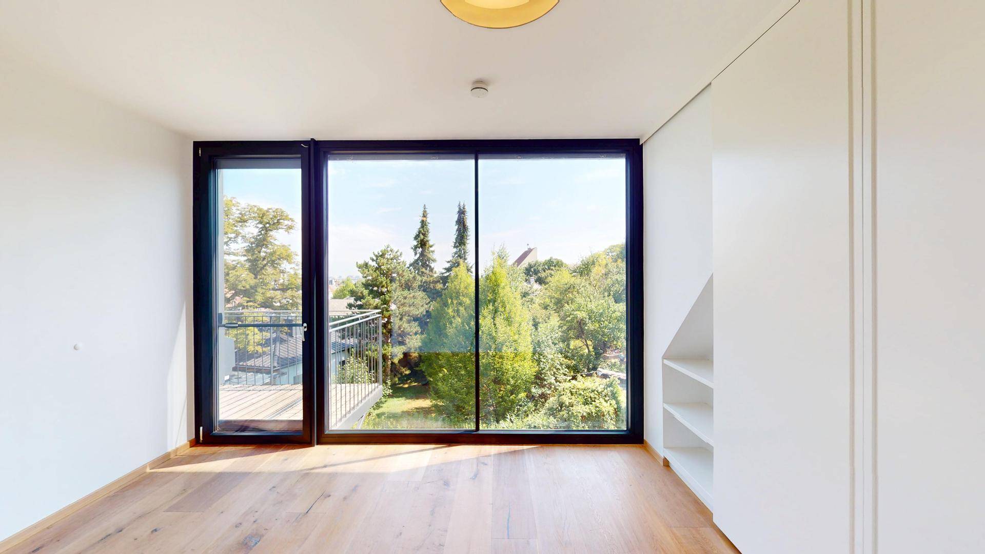 Lichtdurchfluteter Raum mit bodentiefen Fenstern, Holzboden und Einbauregalen, ideal als Schlafzimmer.
