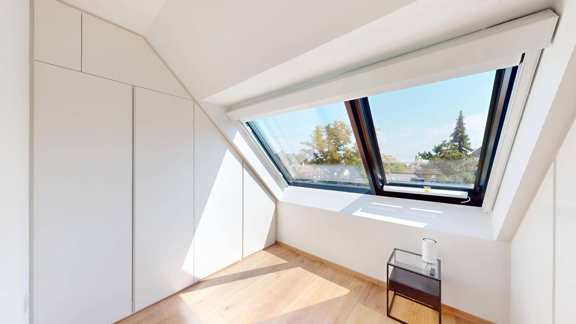 Helles Schlafzimmer mit Dachschrägen, Einbauschränken und einem großen Dachfenster mit Ausblick.