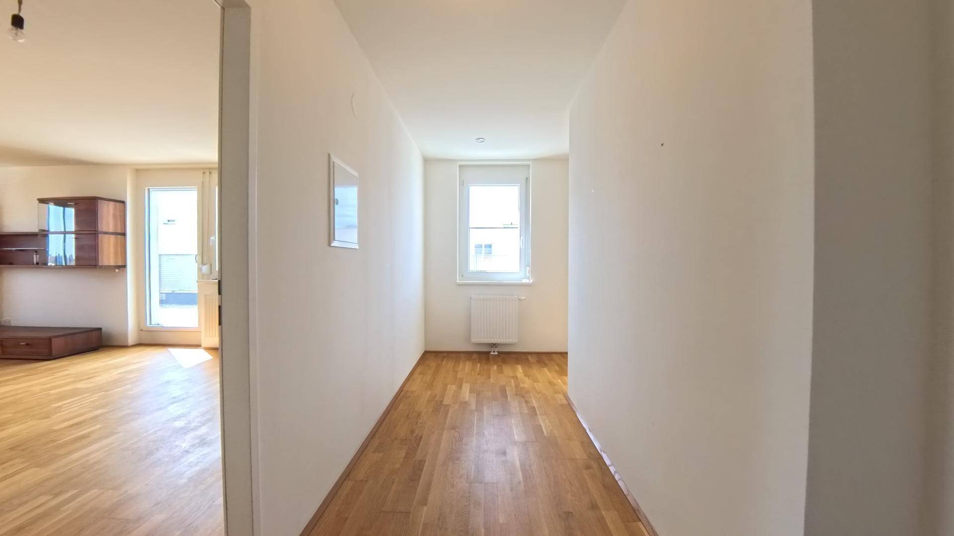 Heller Flur mit Holzparkettboden und einem Fenster am Ende, das viel Tageslicht hereinlässt.