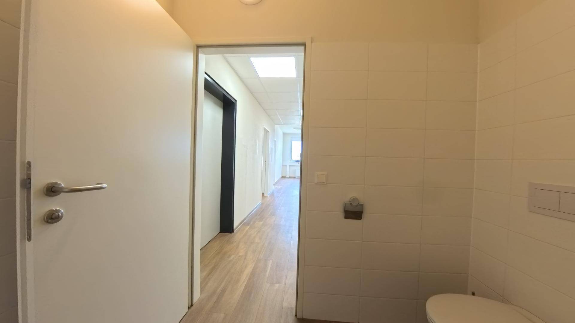 Badezimmer mit weißen Fliesen und Waschbecken, mit Blick in einen angrenzenden Flur.