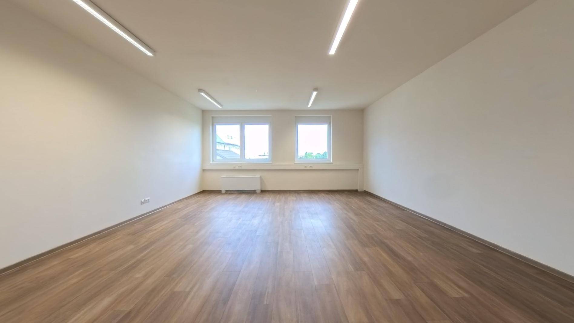 Leerer Büroraum mit zwei Fenstern, Laminatboden und neutralen Wänden, bereit zur Nutzung.