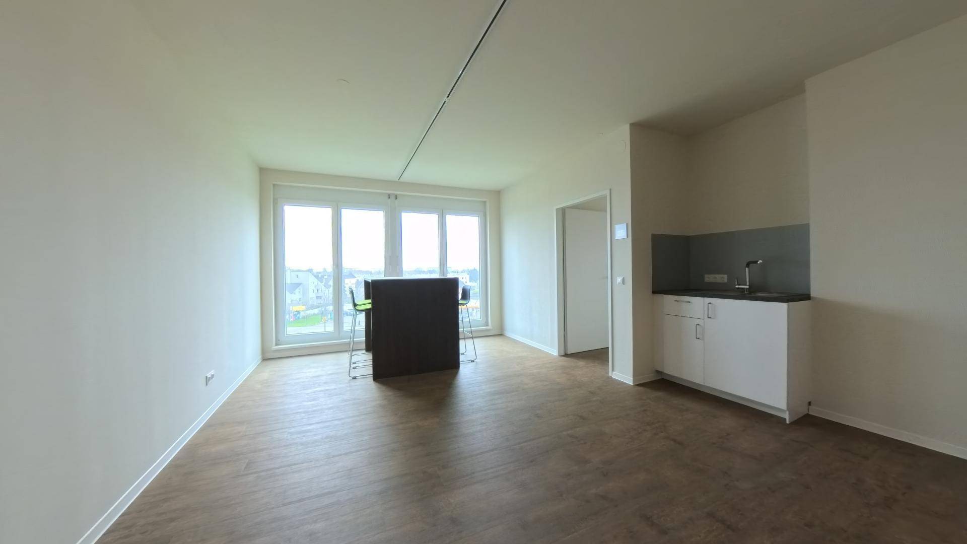 Büro mit kleiner Küchenzeile, großen Fenstern und Holzboden, ideal für Pausen und Besprechungen.