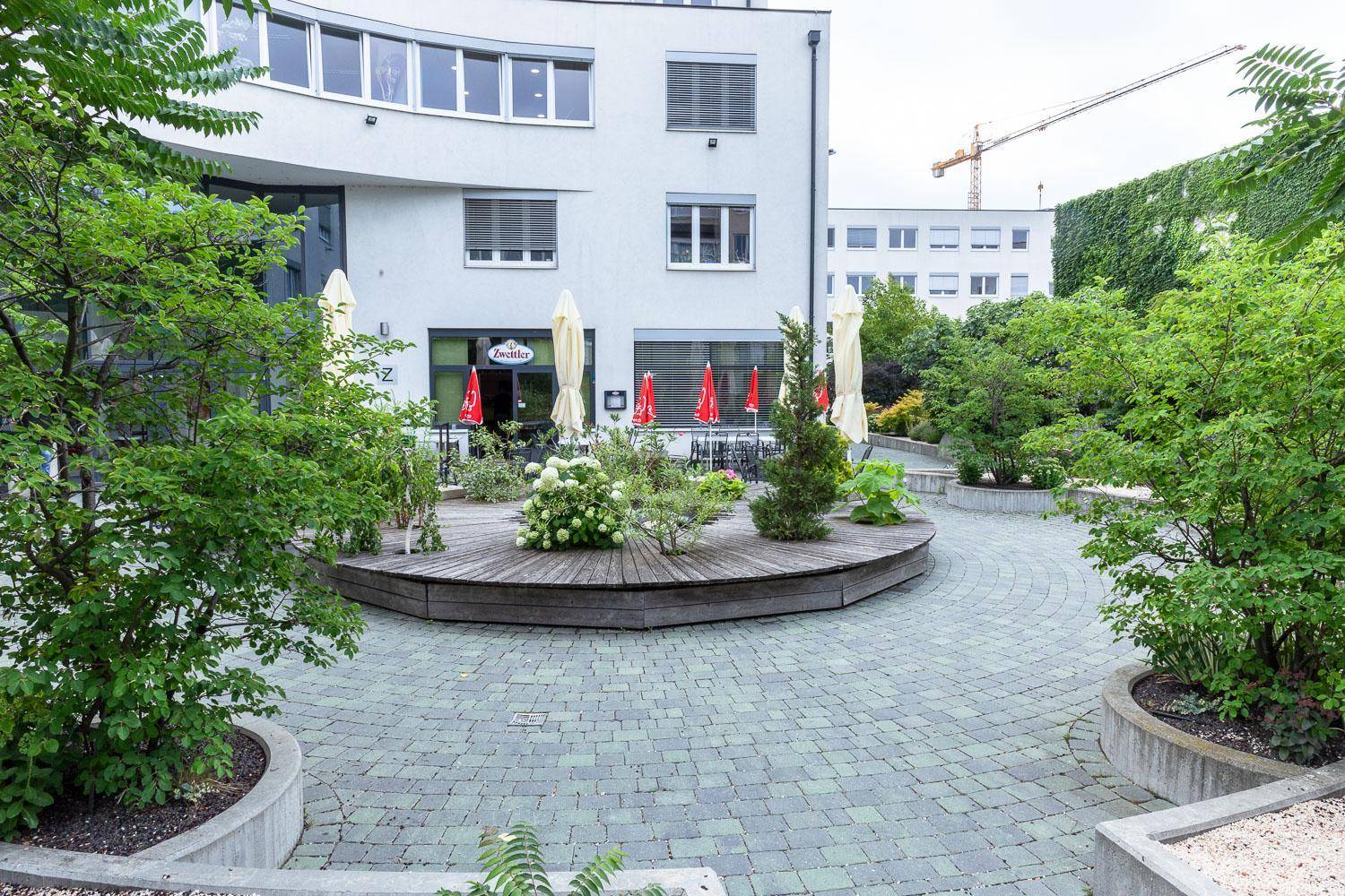 Begrünter Innenhof mit Sitzgelegenheiten und Sonnenschirmen, umgeben von modernen Gebäuden.
