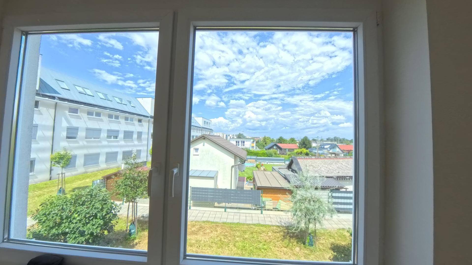Weitblick aus dem Fenster über eine Wohnsiedlung mit Gärten und einem blauen Himmel.