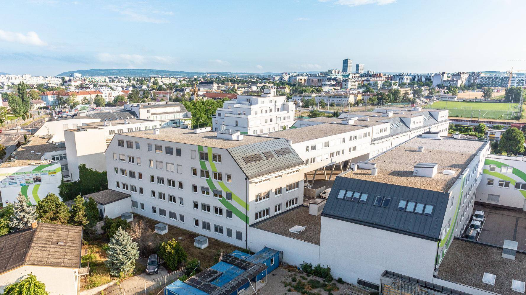 Luftaufnahme eines modernen Bürokomplexes mit grünen Akzenten und städtischer Umgebung unter blauem Himmel.