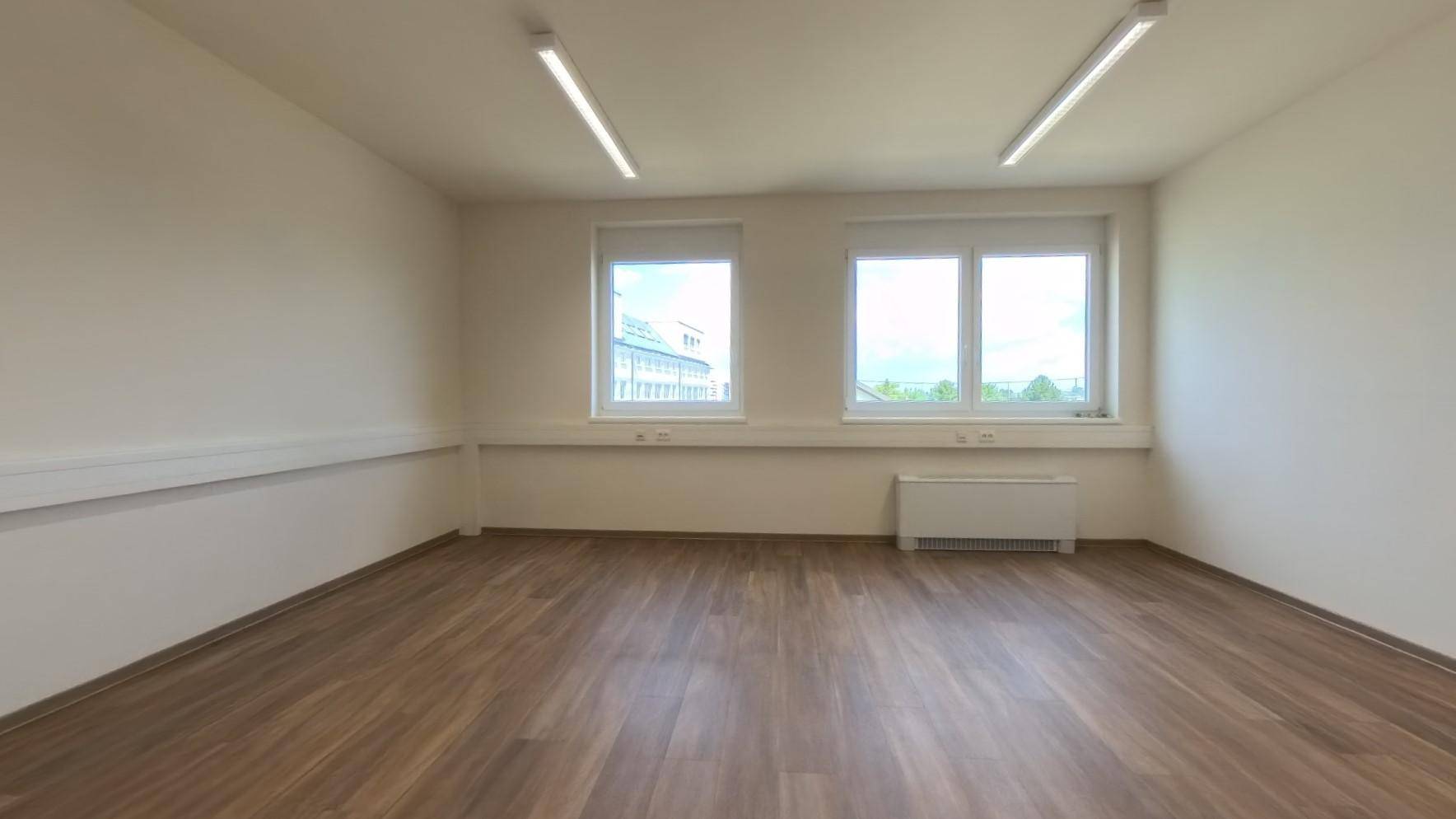 Geräumiger Büroraum mit zwei Fenstern, Laminatboden und neutralen Wänden, bereit zur Nutzung.