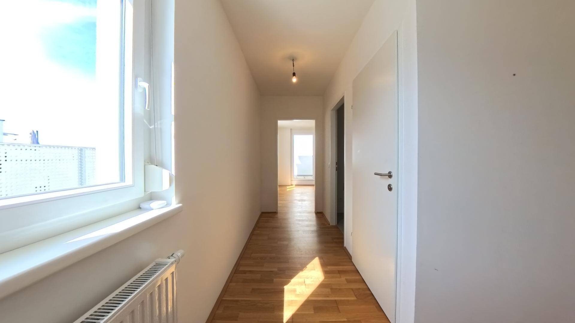 Heller Flur mit Holzparkettboden und einem Fenster, das für natürliche Belichtung sorgt.