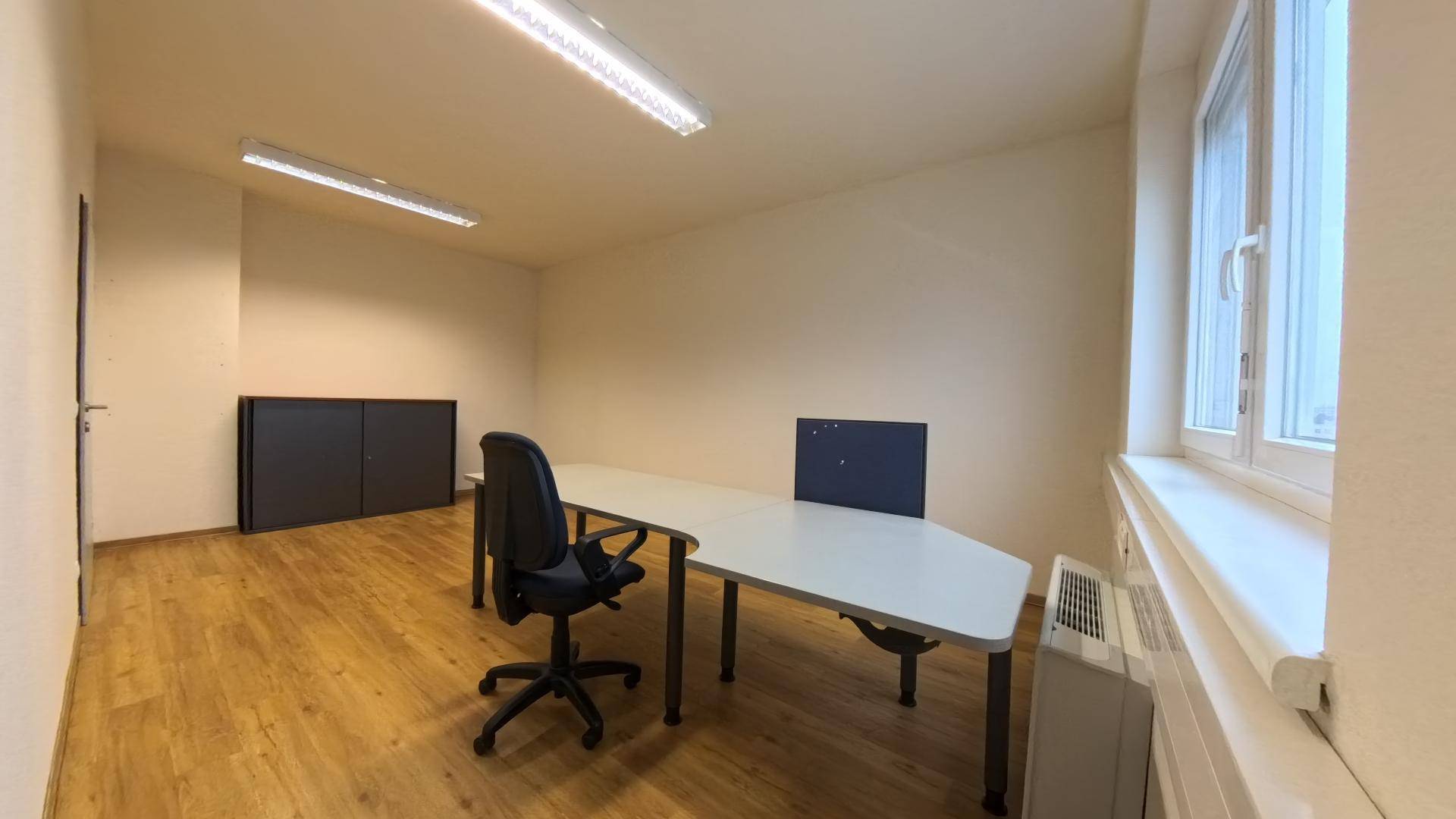 Helles Büro mit Holzfußboden, großem Fenster und einfacher Möblierung für Arbeitszwecke.