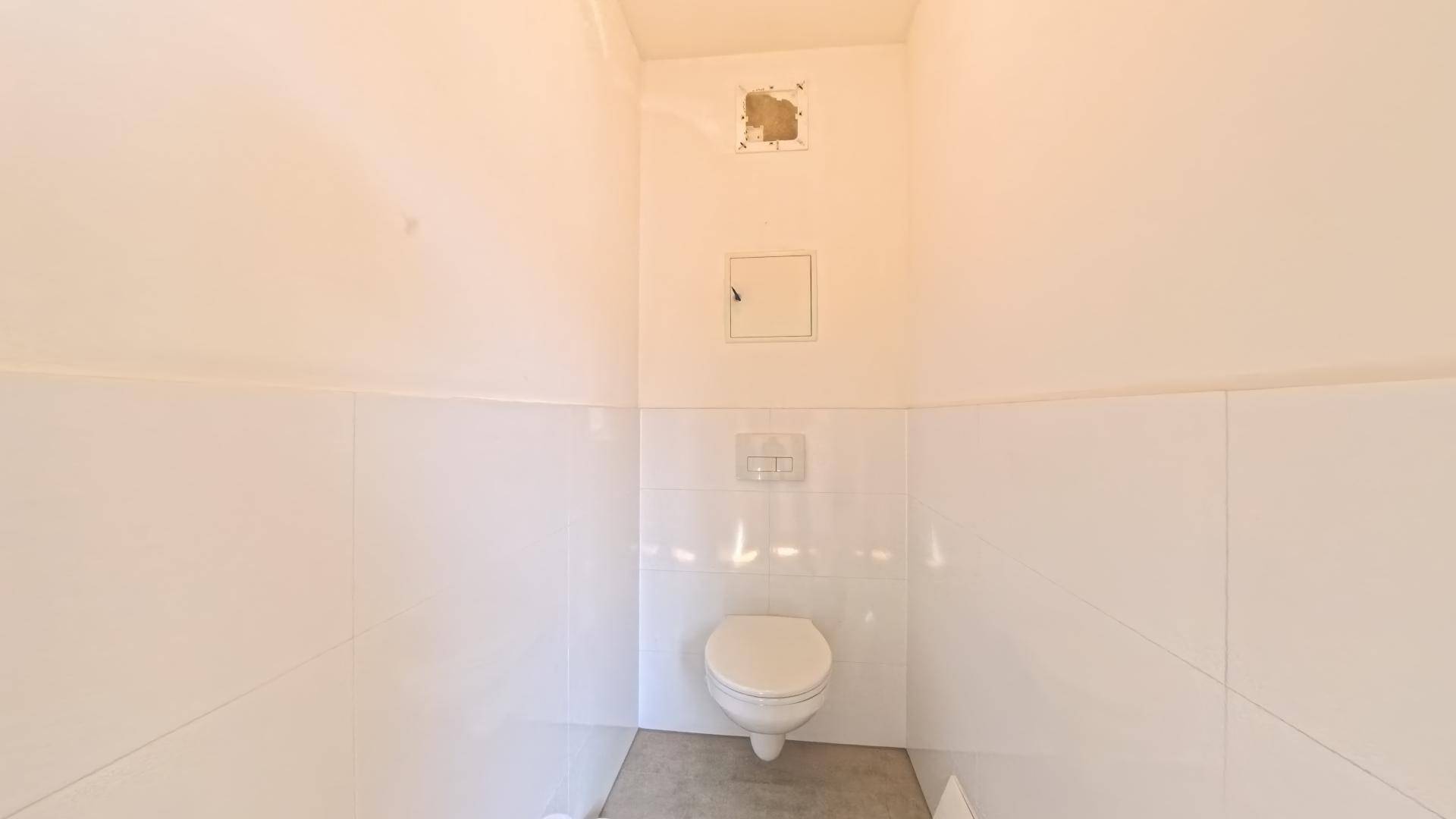 Separates WC mit wandhängender Toilette und weißen Fliesen an den Wänden.