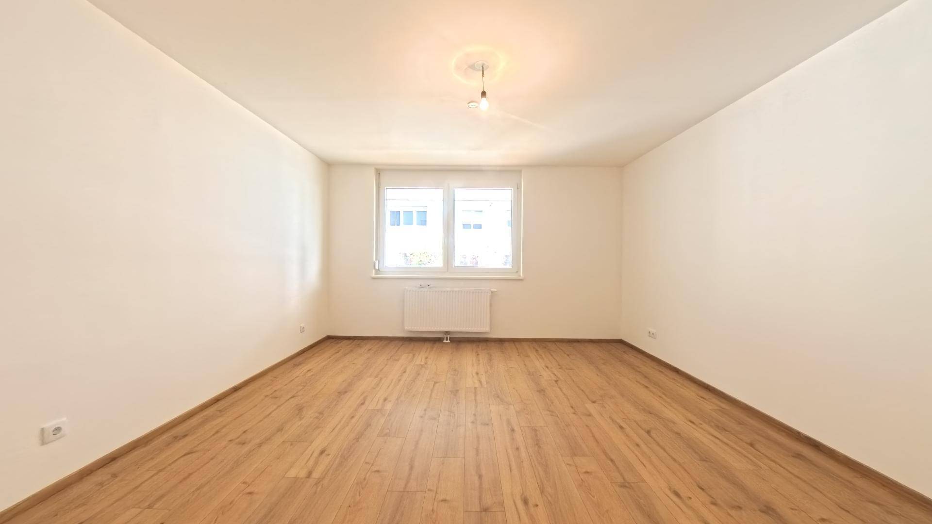 Helles, leeres Schlafzimmer mit Laminatboden und einem großen Fenster.