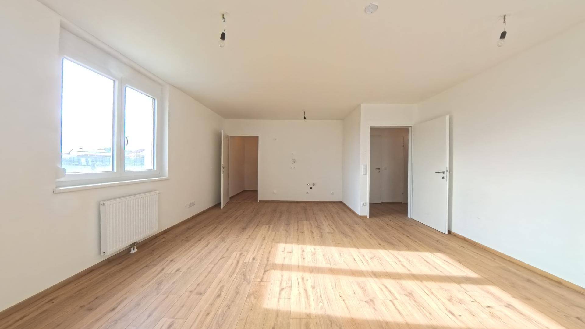 Geräumiges, helles Zimmer mit Laminatboden und mehreren Türen zu angrenzenden Räumen.