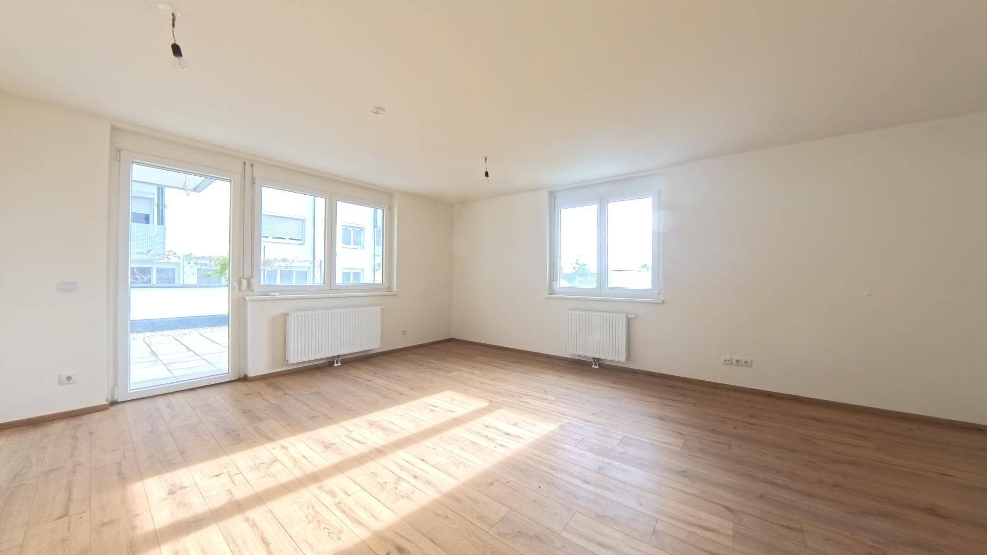 Lichtdurchflutetes Zimmer mit Laminatboden und direktem Zugang zu einer Außenterrasse.