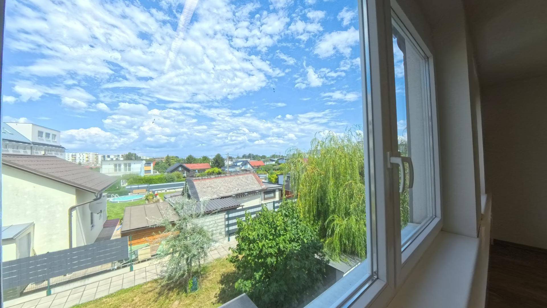 Weitblick aus dem Fenster über eine Wohnsiedlung mit Gärten und einem blauen Himmel.