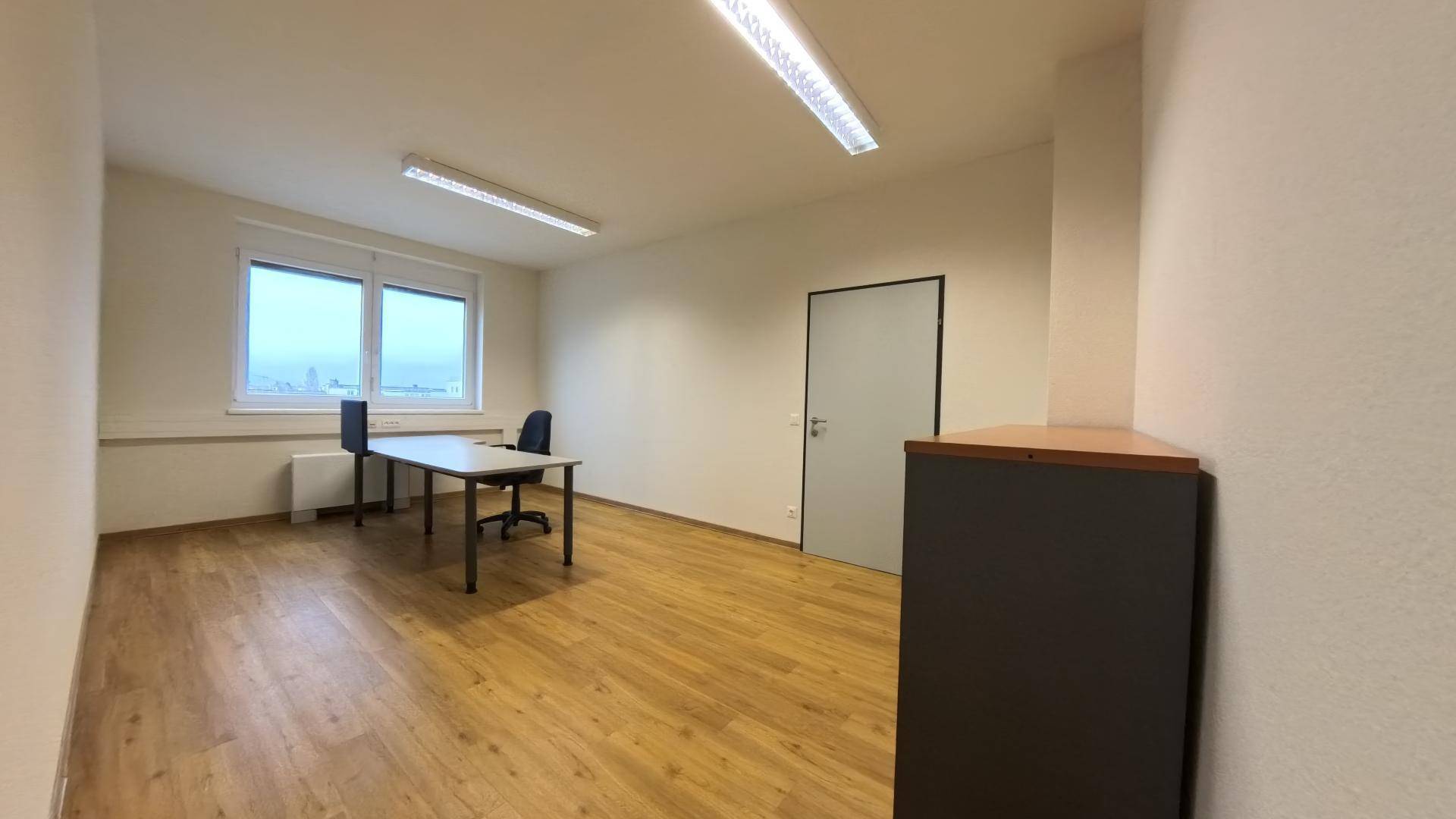 Büro mit Holzfußboden, Schreibtisch und einem praktischen Schrank im Vordergrund für Stauraum.