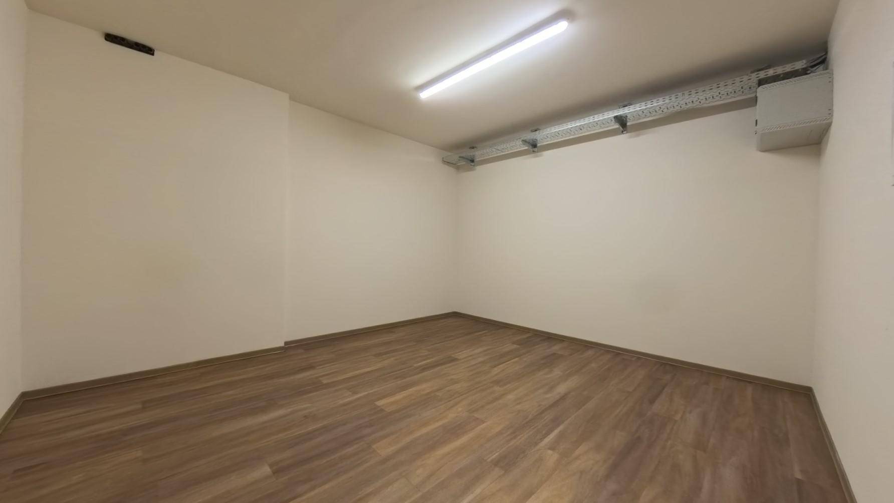 Leerer Büroraum mit Laminatboden und sichtbaren Lüftungsrohren an der Decke.