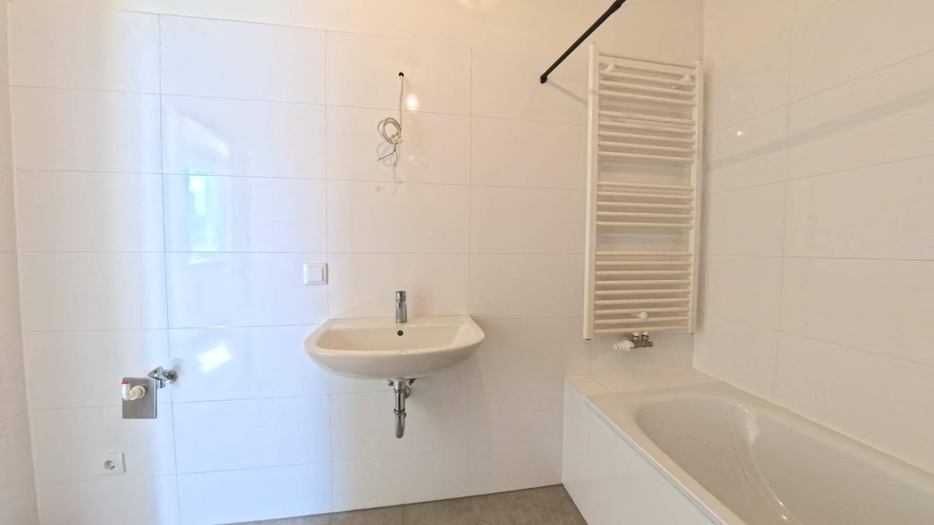 Helles Badezimmer mit weißen Wandfliesen, modernem Waschbecken und Handtuchheizkörper.