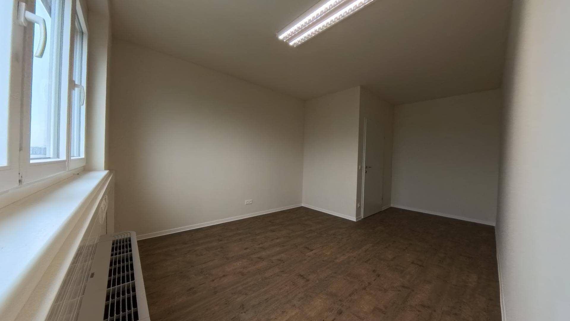 Leeres Büro mit Holzboden, einem Fenster und Heizkörper, in einem gepflegten Zustand.