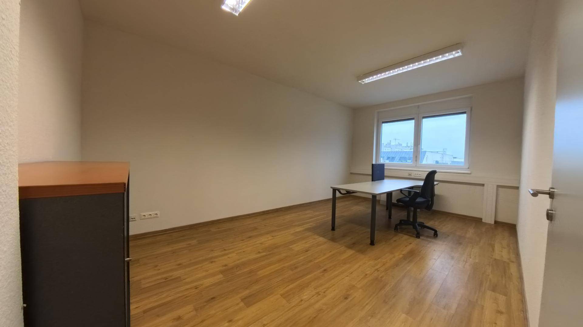 Geräumiges Büro mit Holzfußboden und einem Schreibtisch vor dem Fenster, ideal für konzentriertes Arbeiten.