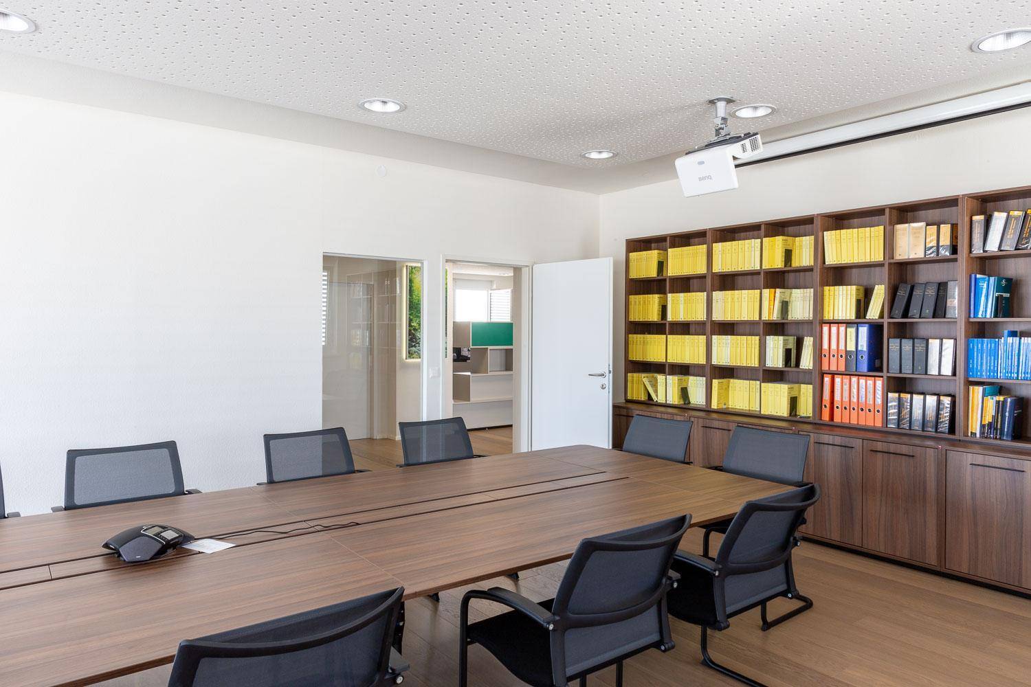 Konferenzraum mit großem Holztisch, ergonomischen Stühlen und einer Wand mit eingebauten Regalen.