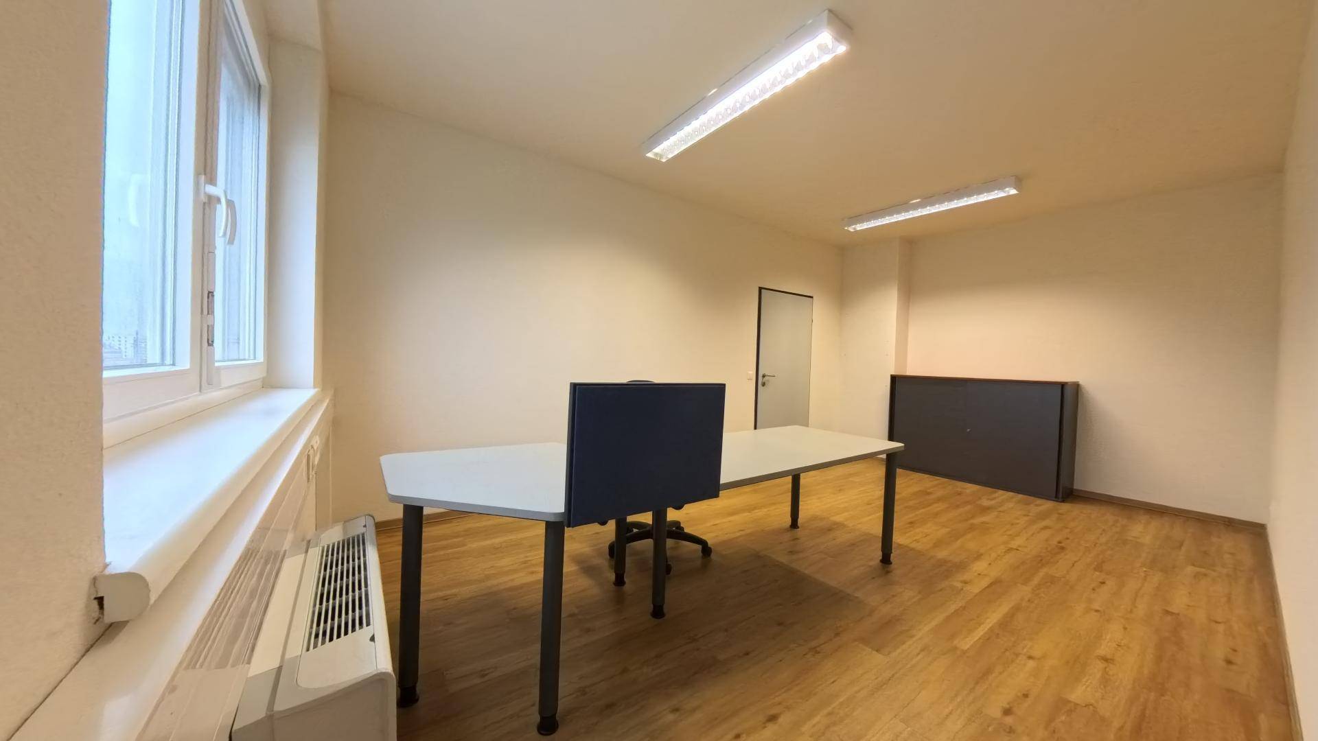 Büro mit Holzfußboden, Schreibtisch und Heizkörper unter dem großen Fenster, sorgt für angenehme Wärme.