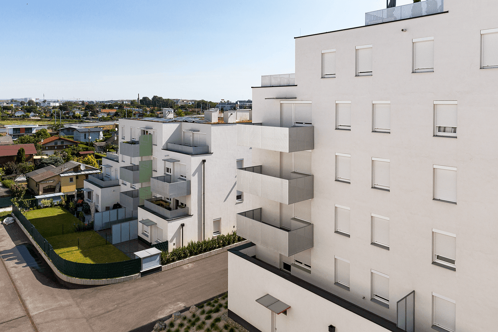 Moderne Wohnanlage mit Balkonen, grünen Außenbereichen und Rollläden an den Fenstern.
