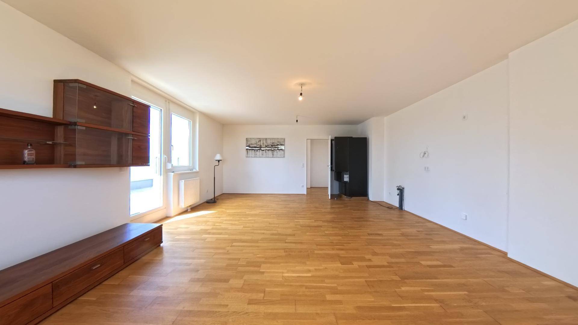 Weitläufiges Wohnzimmer mit Parkettboden, weißen Wänden und viel Platz für individuelle Gestaltung.