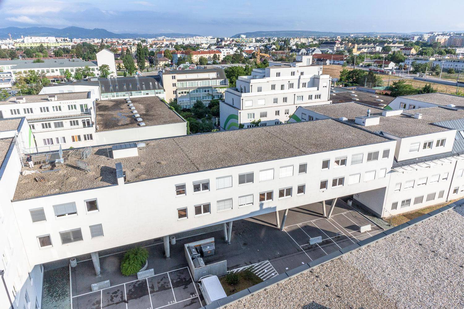 Luftaufnahme eines modernen Gebäudekomplexes mit Flachdächern und umliegender Stadtlandschaft.